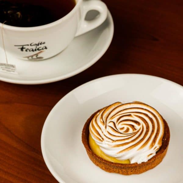 Café allongé accompagné d'une tarte citron meringuée ronde et élégante dans une assiette blanche.