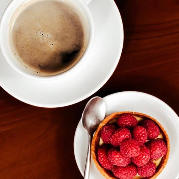Vue de haut d'une subtile tarte au framboise présenté au coté d'un café avec sa mousse légère.